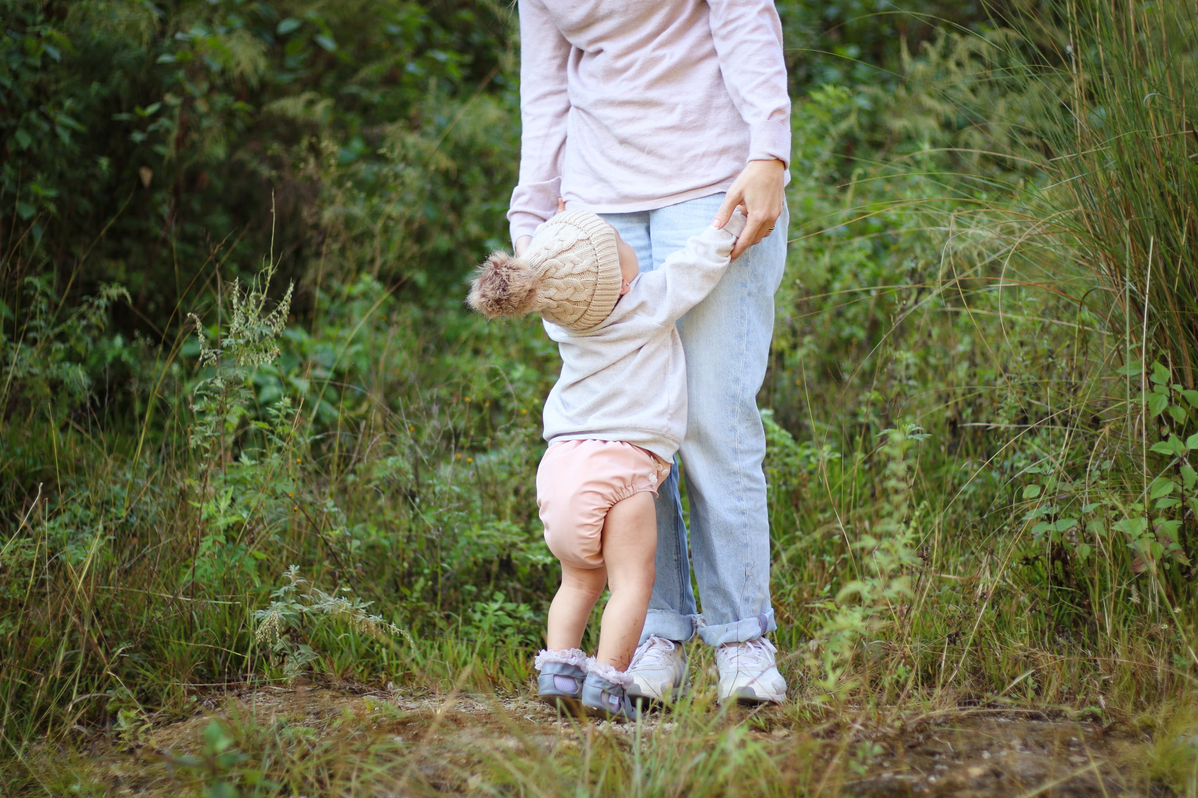 A baby wearing a pink re-usable diaper reaches for her mother to lift her while outdoors