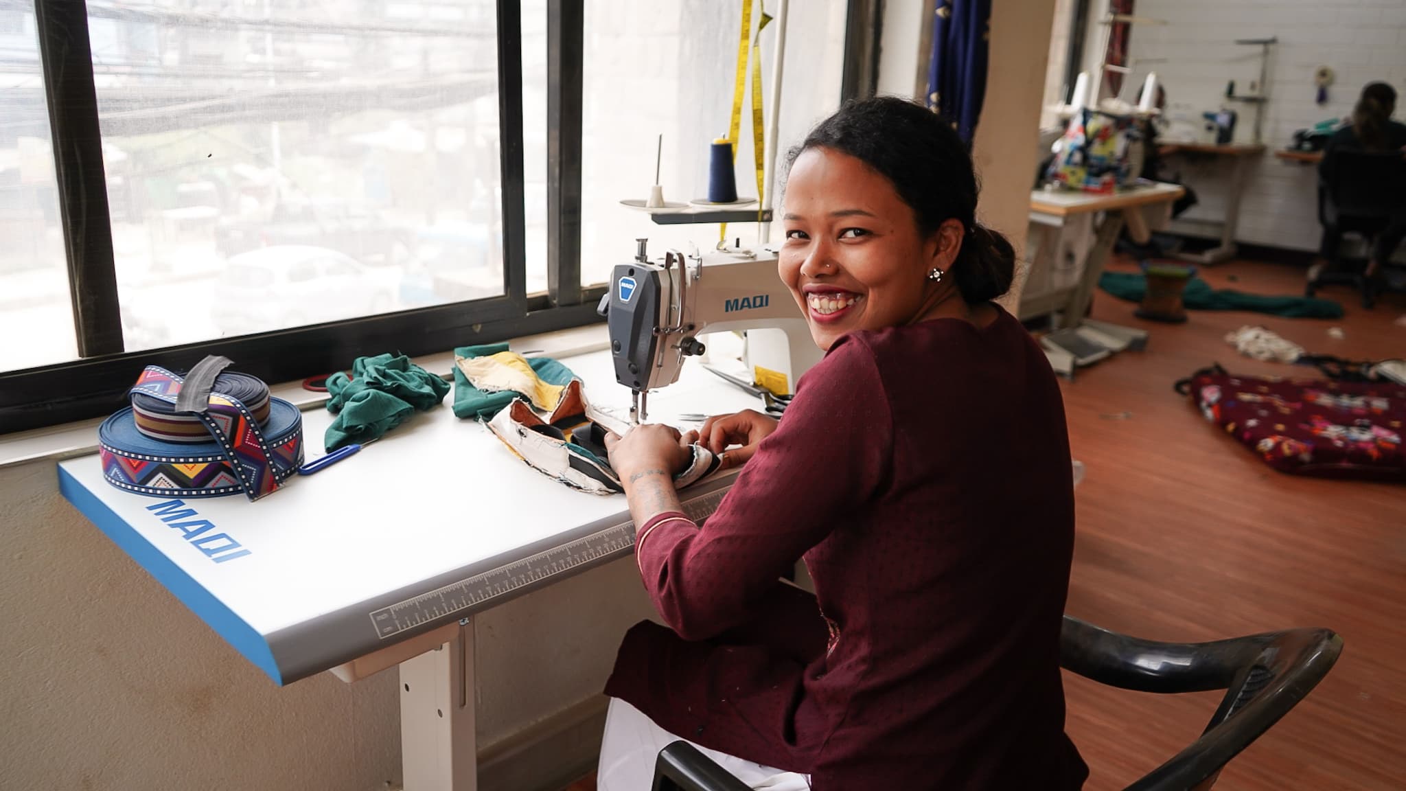 Woman turns to smile while sowing at a machine.