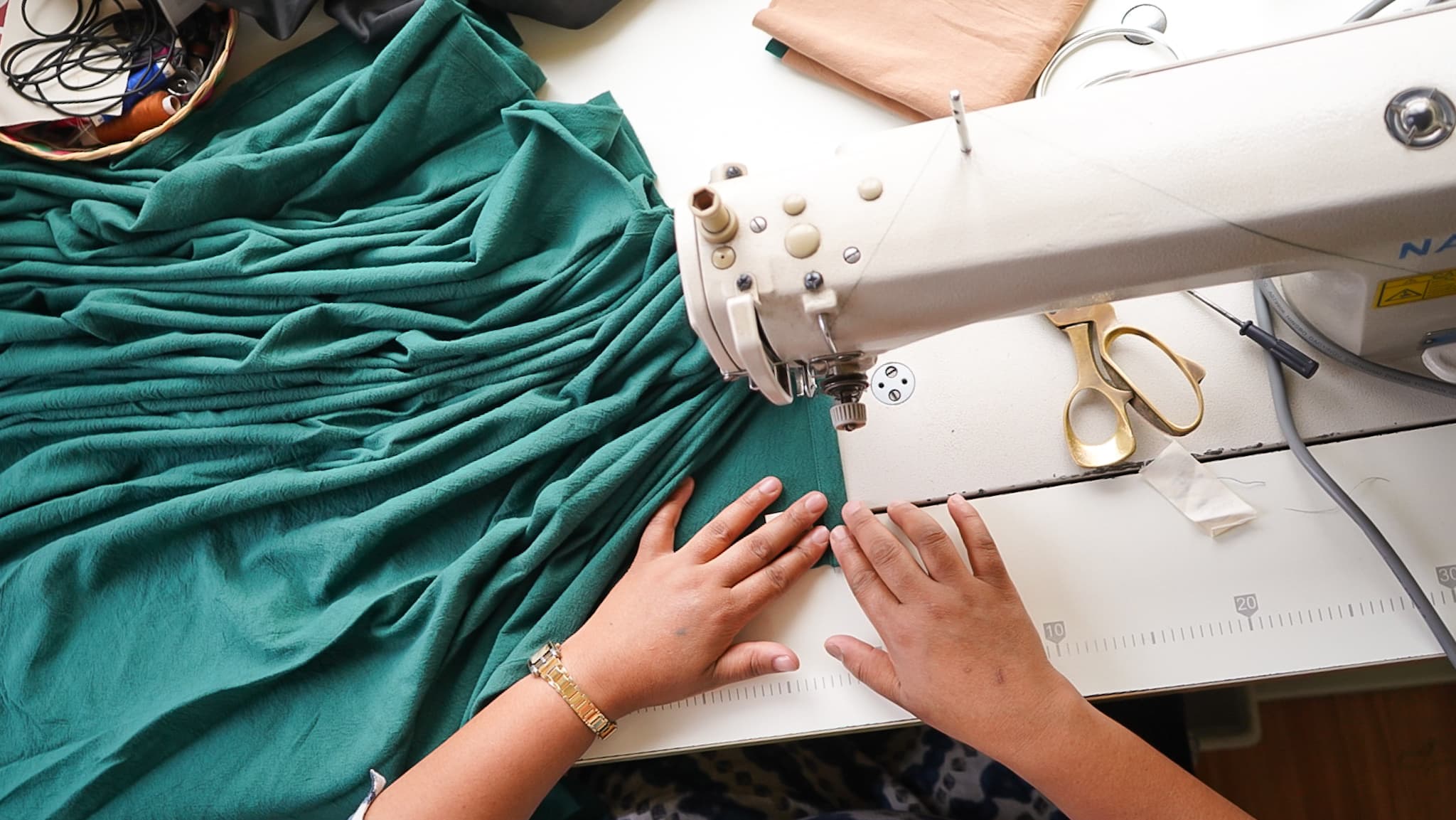 A top-view of a woman's hands sowing green fabric on a modern white sowing machine
